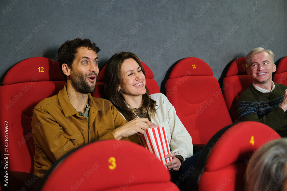 Group of friends watching a movie at the cinema, eating popcorn and having fun