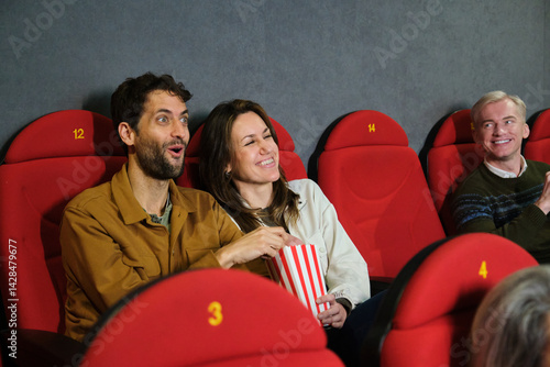 Obraz na płótnie Group of friends watching a movie at the cinema, eating popcorn and having fun w salonie