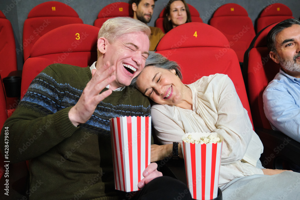 Mature couple laughing and eating popcorn while watching a funny movie at the cinema
