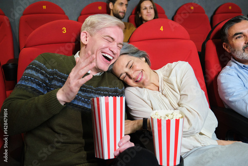 Obraz na płótnie Mature couple laughing and eating popcorn while watching a funny movie at the cinema w salonie