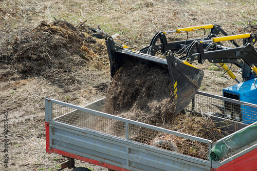 The loader is dumping branches and construction debris into the truck bed — a clear reflection of the importance of waste disposal and ecological responsibility, landscaping the area.