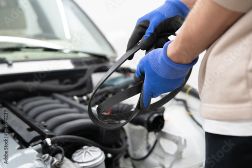 A skilled car mechanic carefully holds a new timing belt while preparing to install it in an engine during routine maintenance.
