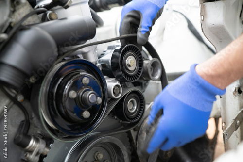 Mechanic Working on Car Timing Belt Replacement Under the Hood in Automotive Workshop