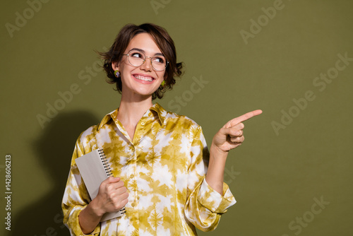 Obraz na płótnie Confident young businesswoman with notebook in hand pointing with a smile against a khaki background w salonie