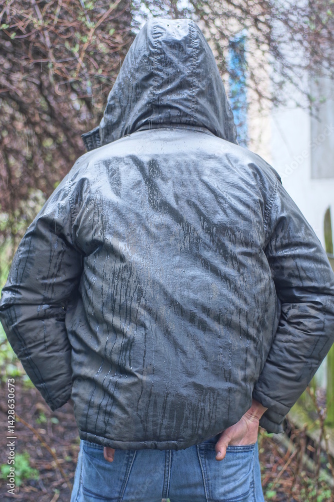 Fototapeta premium one man stands in a gray green wet jacket with a hood on his head in the rain on an autumn street