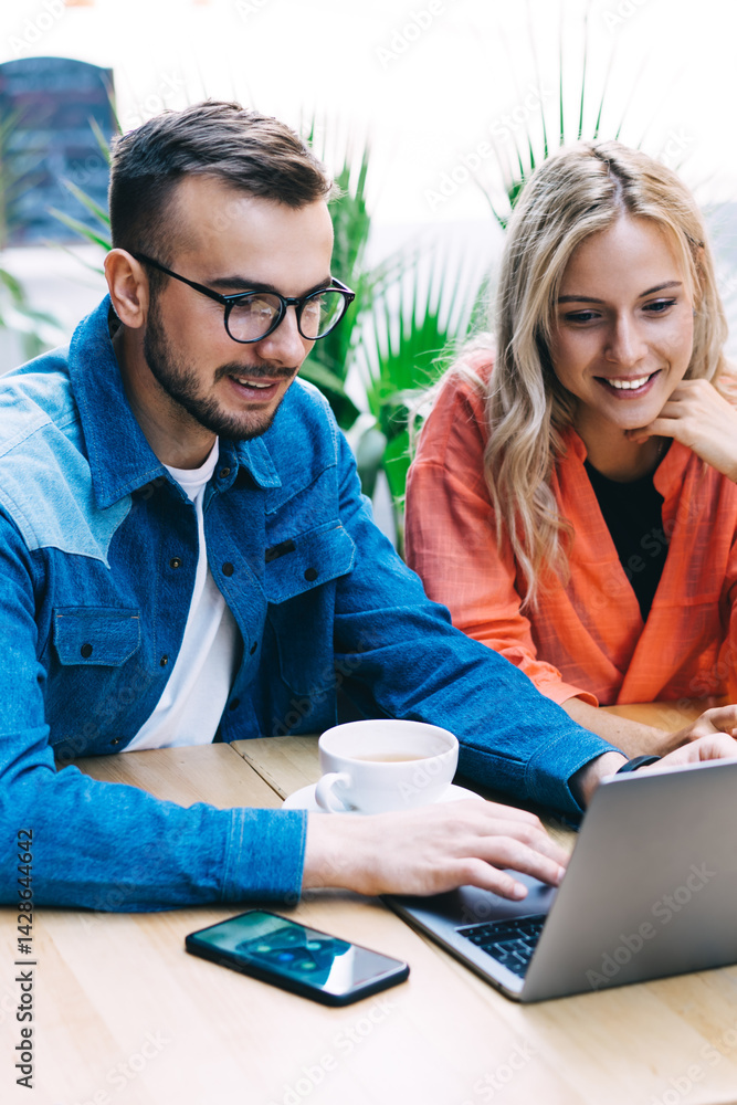 Happy young couple browsing netbook together in summer area of modern cafe