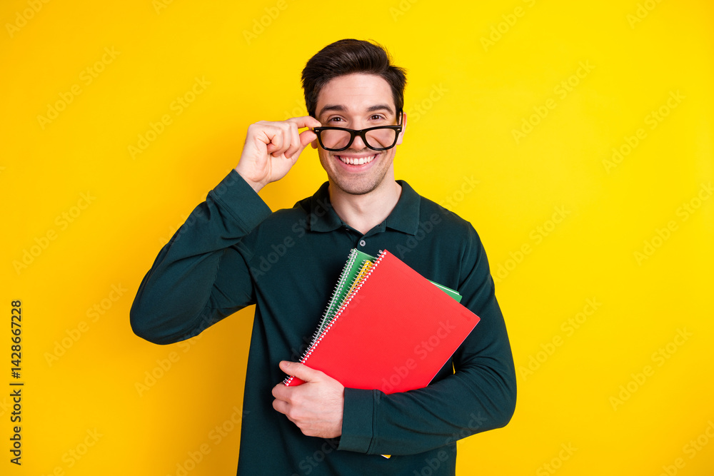 Young man in green polo smiling and holding notebooks against a vibrant yellow background, expressing happiness and confidence. Young man in green polo smiling and holding notebooks against a vibrant yellow background, expressing happiness and confidence.