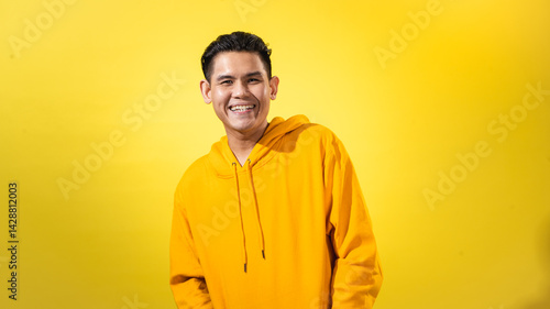 Smiling young Asian man in bright yellow hoodie standing confidently in front of solid yellow background. Cheerful studio portrait with energetic vibe, perfect for modern visual projects
