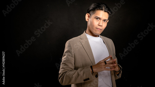 Obraz na plátně Asian man in beige blazer and white t-shirt forming steeple hands gesture with c