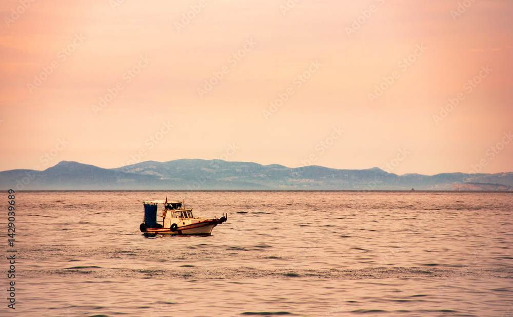 Fototapeta premium A very small fishing boat on a grey and calm sea and under a red sky. Beautiful dusk view in evening.