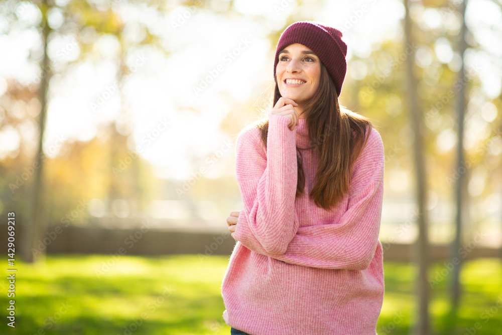 Smiling woman in a cozy pink sweater looking thoughtful in the park Smiling woman in a cozy pink sweater looking thoughtful in the park