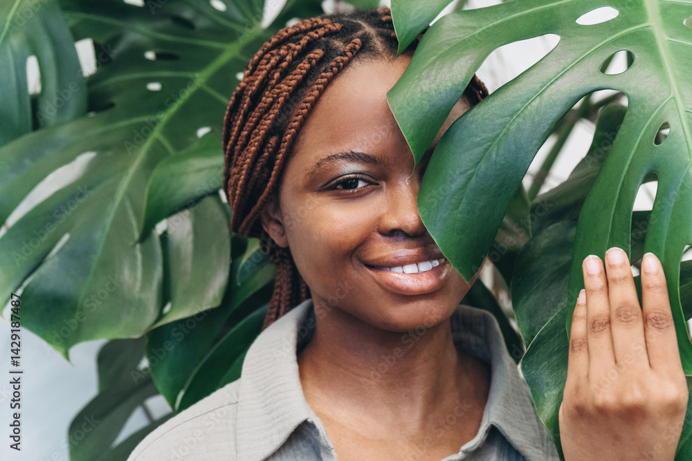 A smiling woman whose radiance shines through the green leaves in an exquisite home environment