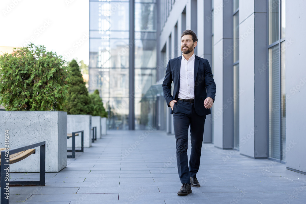 A well-dressed businessman walks confidently in a modern urban setting, exuding professional ambition. He is wearing a dark suit.