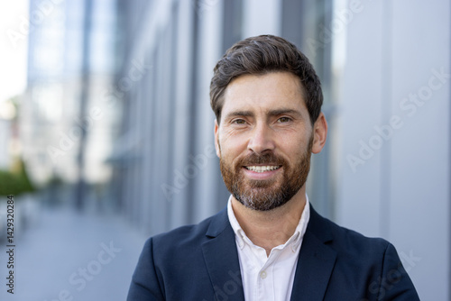 Obraz na płótnie A smiling businessman poses outside of an office building. He is wearing a suit and looking at the camera with a friendly expression. w salonie
