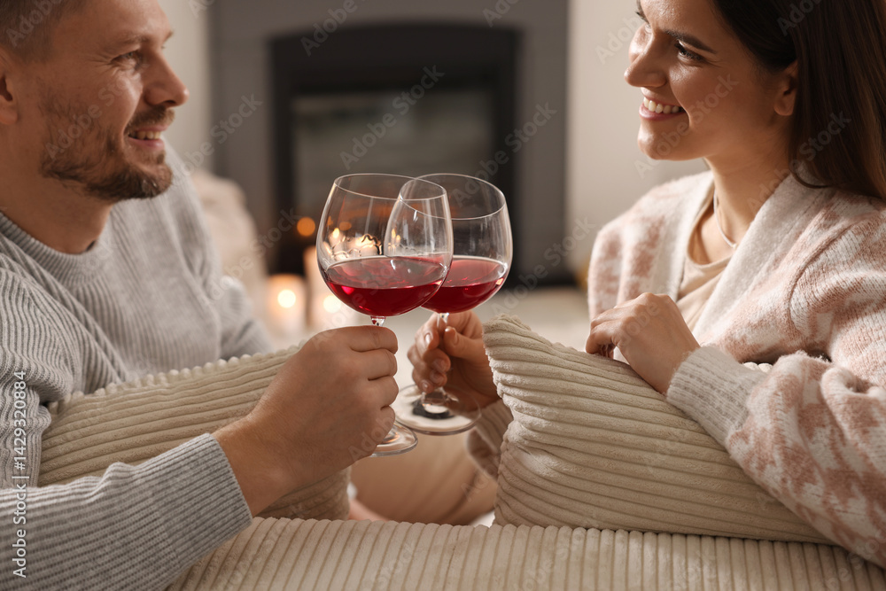 Happy couple clinking glasses of wine on sofa in room with stylish fireplace