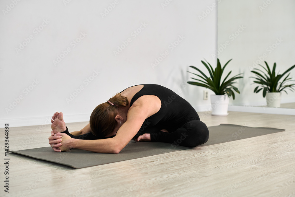 Young woman with brown hair performs yoga forward bend on mat. Minimalistic room with potted plants enhances calm ambiance. Soft light accentuates serene mood Young woman with brown hair performs yoga forward bend on mat. Minimalistic room with potted plants enhances calm ambiance. Soft light accentuates serene mood