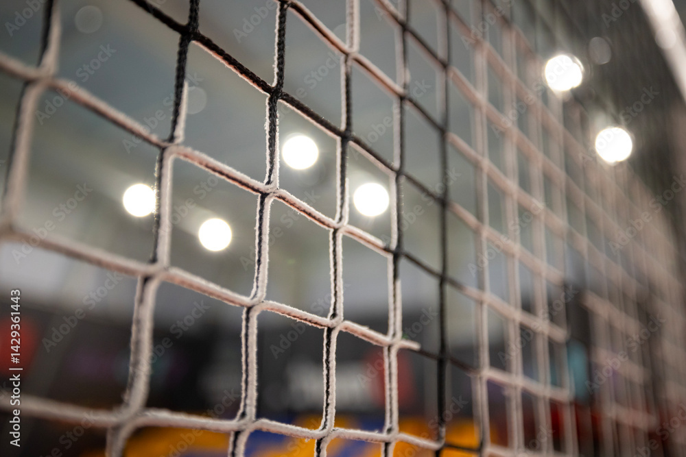 Φωτογραφία Close-up of a square-patterned black volleyball net with a blurred background showing indistinct colorful shapes and bright lights in an indoor volleyball arena