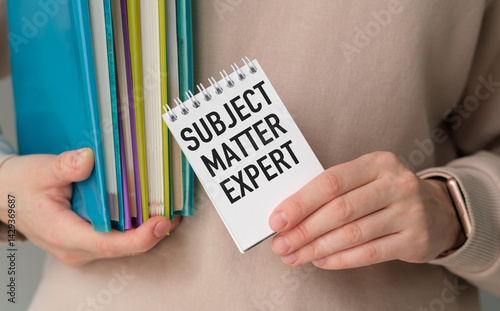 A person is holding a stack of books and a notebook with the words Subject Matter Expert written on it