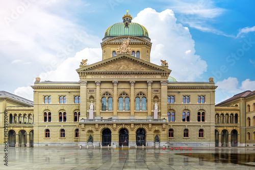 Iconic Renaissance Revival architecture of the Federal Palace in Bern, Switzerland's seat of government, reflected perfectly on the wet Bundesplatz under a beautiful blue sky