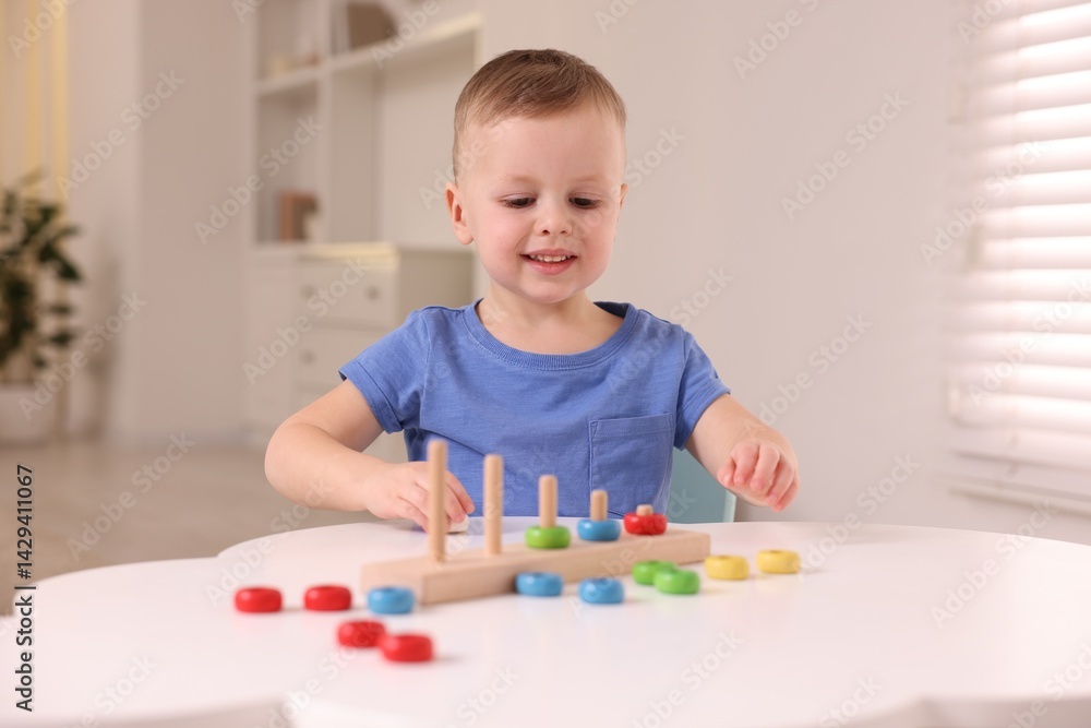Motor skills development. Little boy playing with stacking toy at white table indoors Motor skills development. Little boy playing with stacking toy at white table indoors