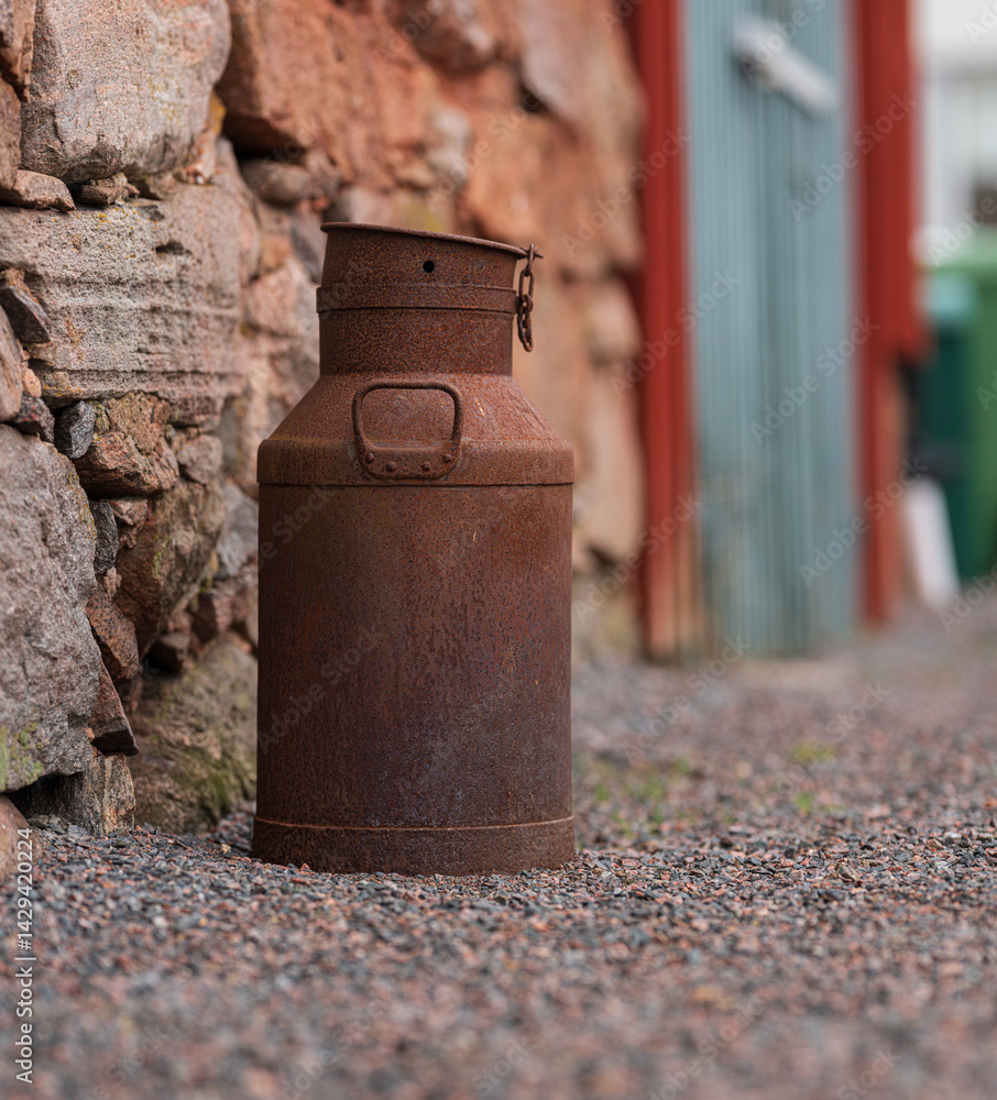Obraz premium Rusty metal milk can against stone wall.