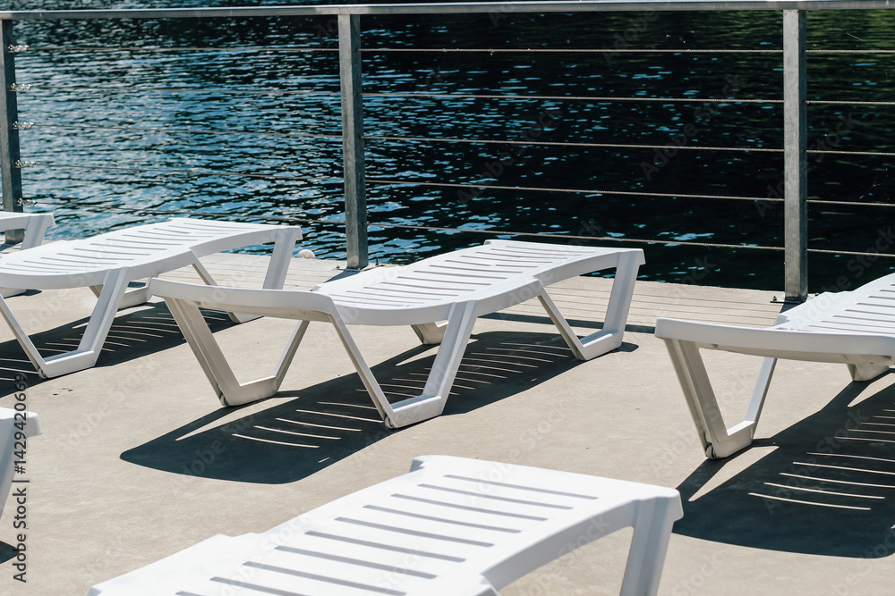 Fototapeta premium Serene lakeside relaxation with white loungers under gentle sunlight