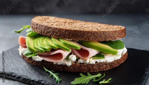 ham sandwich with cream cheese green salad avocado and rye bread on a black marble board dark grey background close up