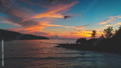 Obraz na płótnie Orange, pink and blue sunset sky over Koh Ma Beach in Koh Phangan, Thailand, with tourists walking along the sandbar at low tide, connecting Koh Ma to the main island w salonie