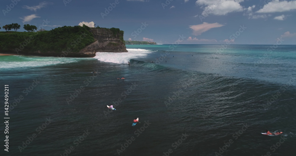 Stunning aerial view of surfers riding waves at the famous Dreamland Beach on Bali island, Indonesia, with a dramatic cliff in the background and turquoise water