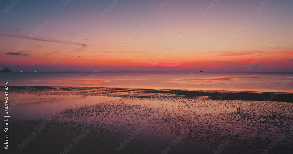 Colorful sunset reflecting on the wet sand of sand beach, with tourists walking along the shoreline, creating a serene and picturesque atmosphere filled with tranquility and beauty. Natural background