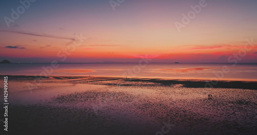 Obraz na płótnie Colorful sunset reflecting on the wet sand of sand beach, with tourists walking along the shoreline, creating a serene and picturesque atmosphere filled with tranquility and beauty. Natural background w salonie