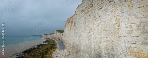Obraz na płótnie Seven Sisters chalk cliffs in the UK with dramatic coastal drop, tidal beach, and people walking along the shoreline w salonie
