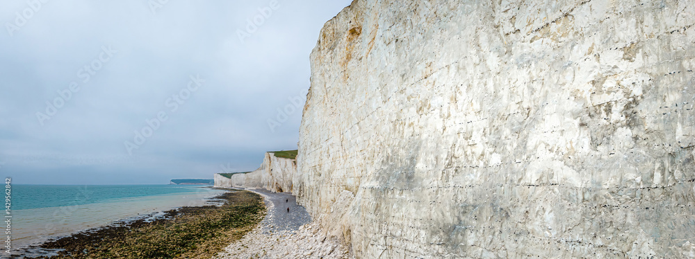 Seven Sisters chalk cliffs in the UK with dramatic coastal drop, tidal beach, and people walking along the shoreline