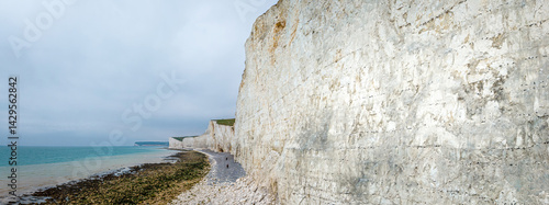 Obraz na płótnie Seven Sisters chalk cliffs in the UK with dramatic coastal drop, tidal beach, and people walking along the shoreline w salonie