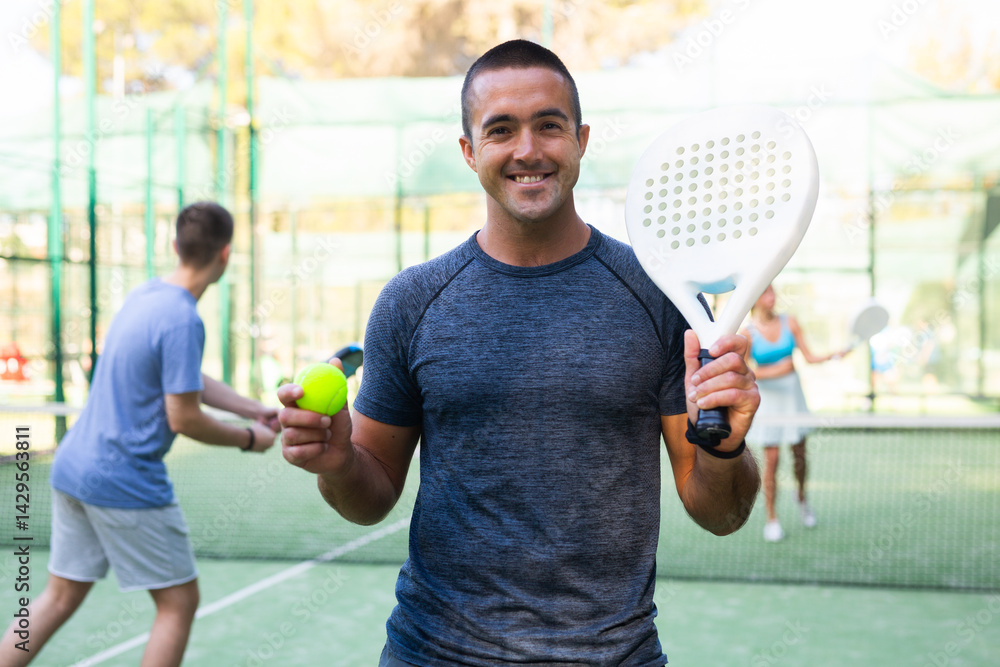 Fototapeta premium Portrait of a satisfied adult man with racket and ball in his hands on the padel court