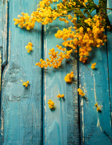 A vibrant bouquet of yellow mimosa blossoms rests on a rustic blue wooden surface. Generative AI