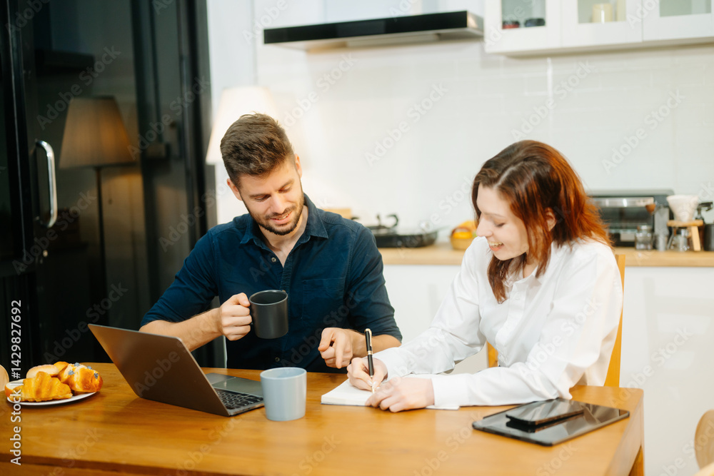Obraz premium Modern couple collaborating over coffee in a cozy kitchen setting with a laptop, notebook, and breakfast.
