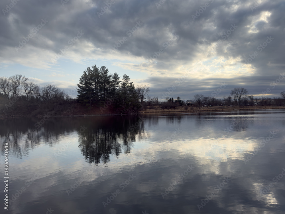 Obraz premium Sunset at the lake with reflections of trees and clouds in the water