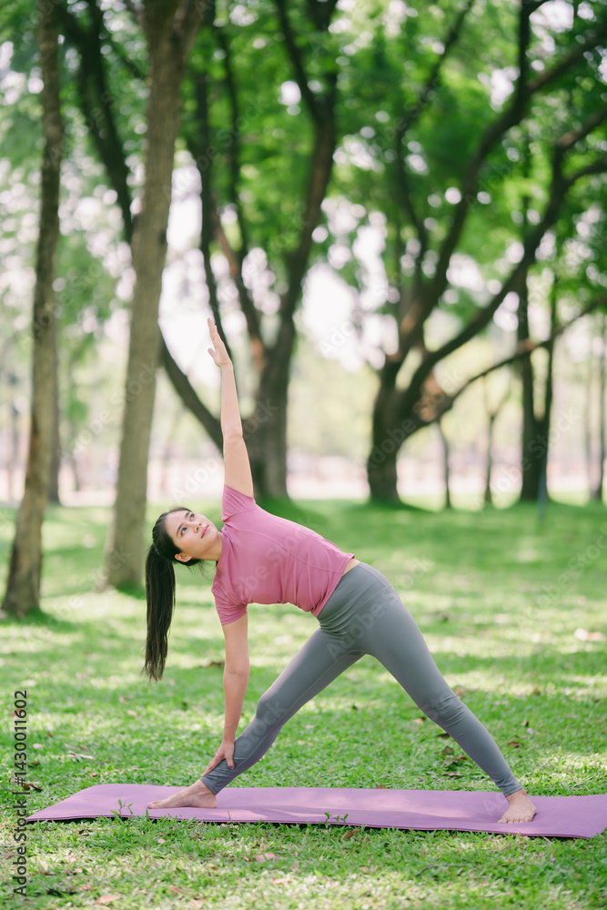 Fototapeta premium Warrior pose, Asian woman with a slim figure standing and doing deep stretches and yoga in a public exercise, focus on a specific point.