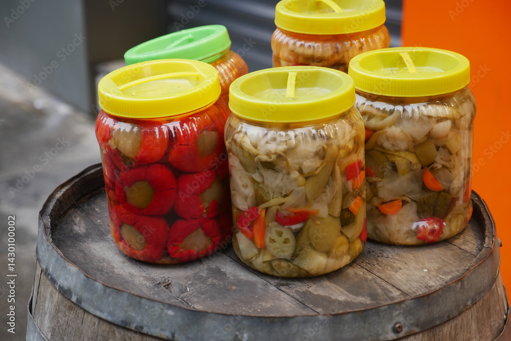 Vibrant jars of pickled vegetables on a wooden barrel in a market Vibrant jars of pickled vegetables on a wooden barrel in a market