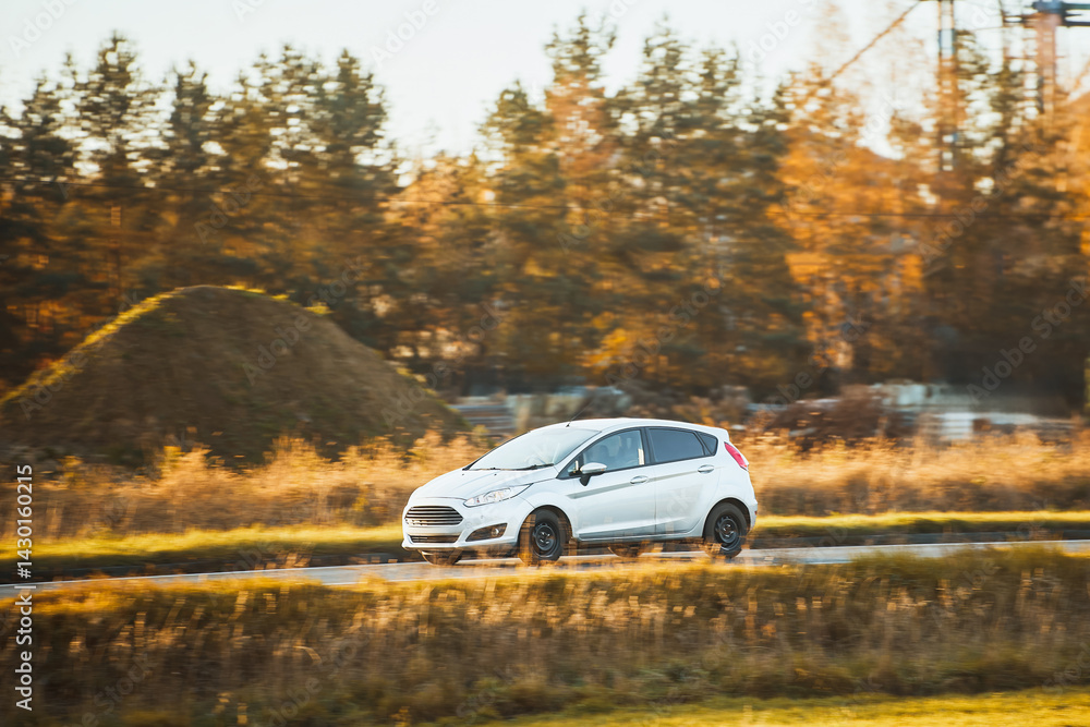 White compact car driving near industrial site