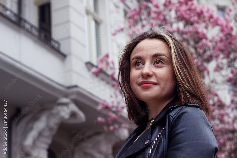 Portrait of a pretty young brunette woman with brown eyes under blooming pink magnolia flowers