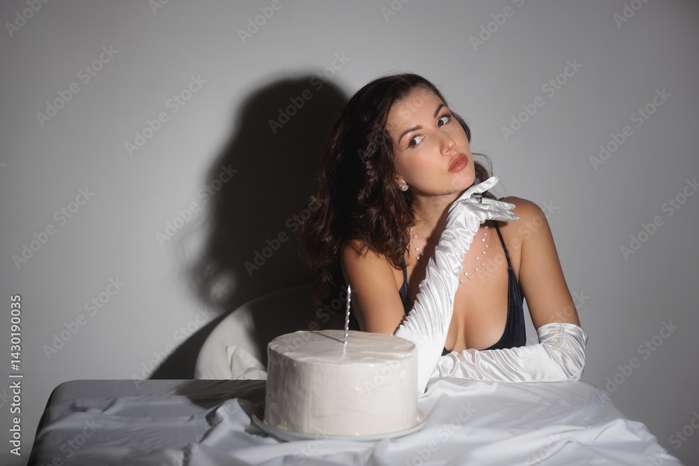 A glamorous woman in white gloves and a black top poses elegantly with a birthday cake and a lit candle. This high-quality stock photo is perfect for promoting luxury, elegance, and sophistication in