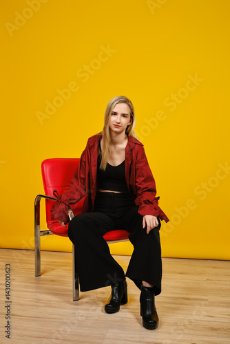 Wallpaper Mural Young woman seated on a red chair against a vibrant yellow background in a modern setting Torontodigital.ca