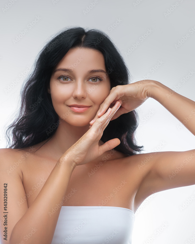 Close-up portrait of an elegant young woman with dark hair, smooth skin, and a natural look, gracefully posing with hands framing her face. Perfect for beauty, skincare, and wellness promotions.