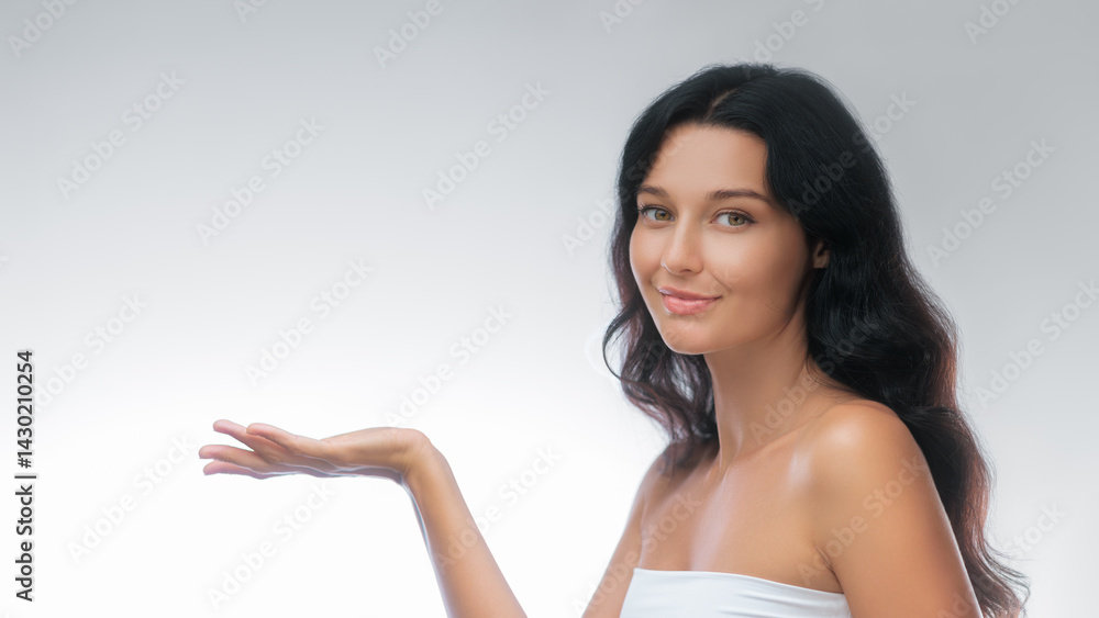 Portrait of a young woman with dark hair and clear skin, holding her hand up as if presenting something, against a clean white background. Perfect for advertising, beauty, and lifestyle concepts.