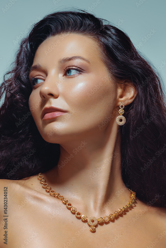 Glamorous studio portrait of a confident woman with wavy hair, glowing skin, and luxurious gold necklace and earrings. Ideal for fashion, jewelry ads, and beauty campaigns.
