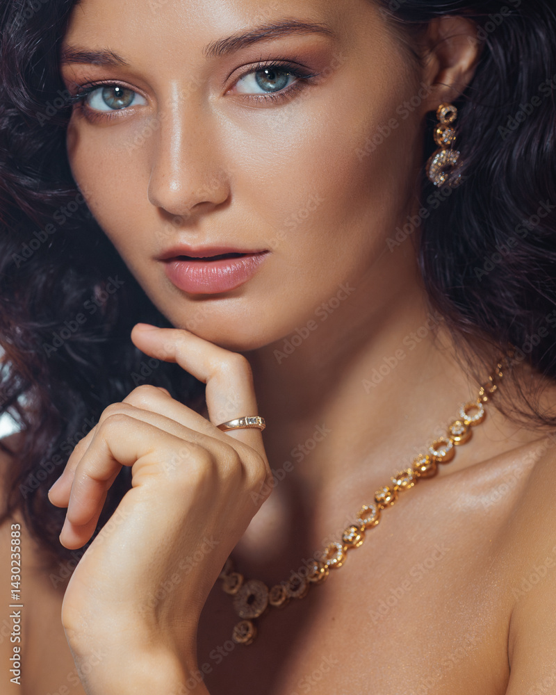 Stunning woman with glowing skin, gold necklace, earrings, and subtle makeup in a studio portrait. High quality beauty image perfect for fashion, cosmetics, and luxury branding.
