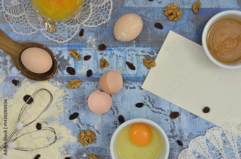 Ingredients for baking, lots of ingredients and a blank piece of paper to write the recipe. Top view blue table and embroidered, retro napkins.
