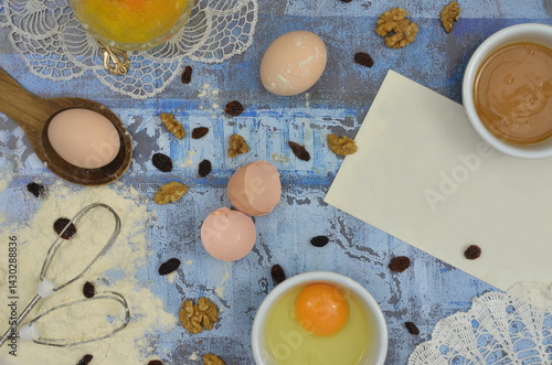 Obraz na płótnie Ingredients for baking, lots of ingredients and a blank piece of paper to write the recipe. Top view blue table and embroidered, retro napkins. w salonie